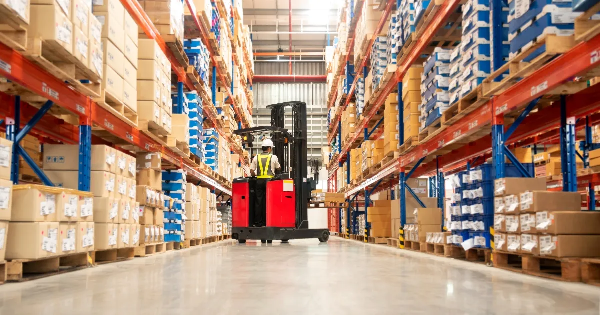 Forklift operator in warehouse aisle with stacked pallets