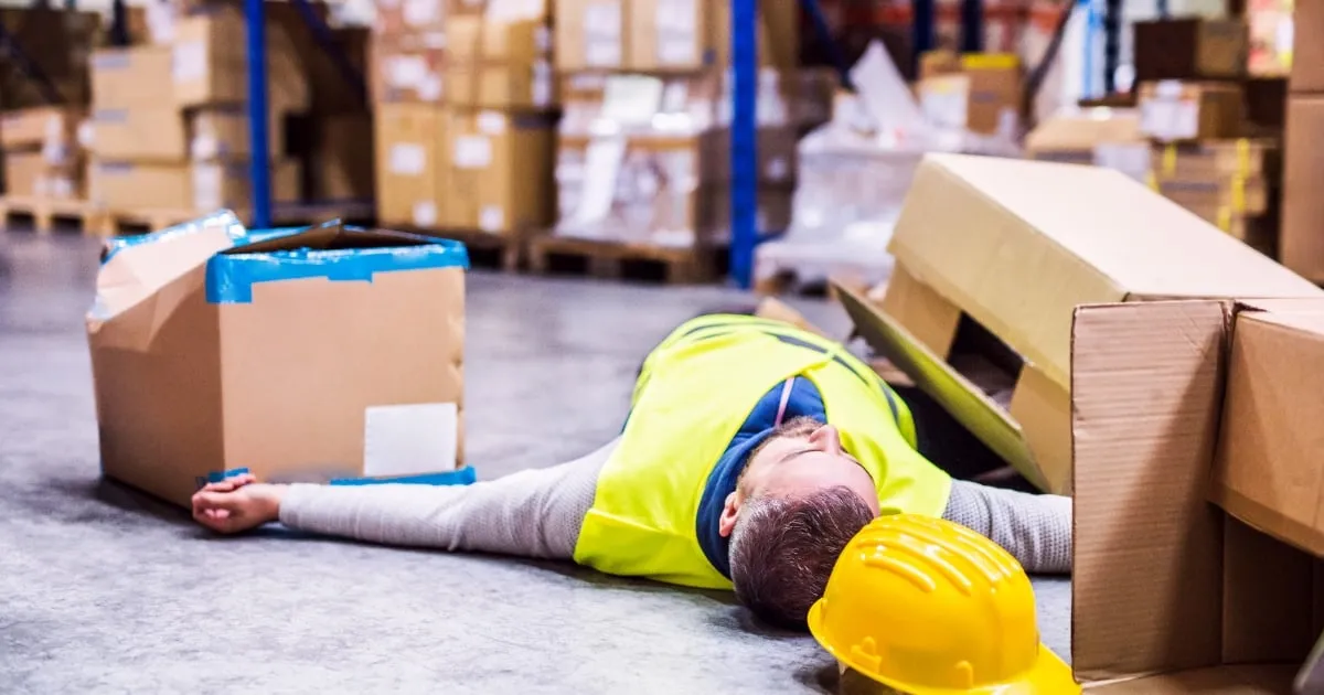 Injured warehouse worker lying beside fallen boxes