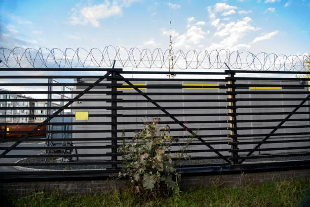A high-security black metal slatted fence topped with coiled razor wire