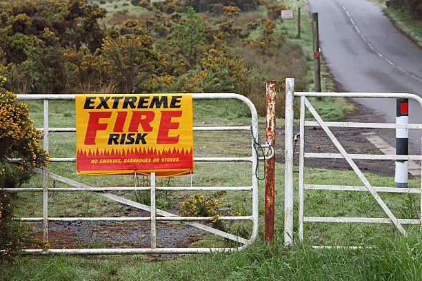 A bright yellow and red 'EXTREME FIRE RISK' warning sign attached to a white metal farm gate