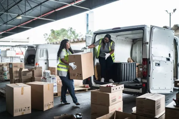 Workers unloading boxes from delivery van in warehouse