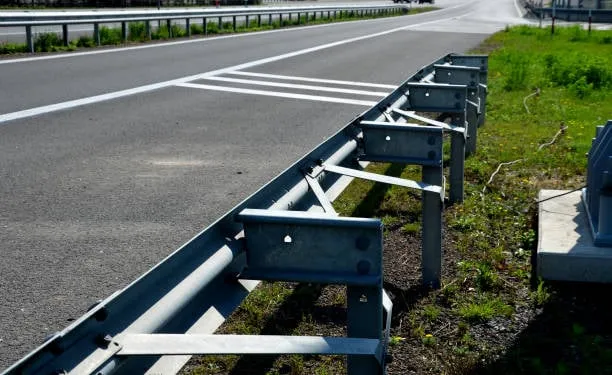 A close-up view of a metal guardrail system installed along the shoulder of a paved highway.
