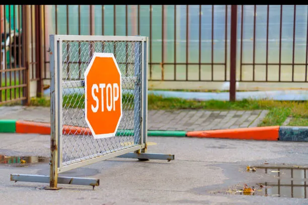 A portable chain-link barrier with a bright orange octagonal 'STOP' sign positioned on a paved road