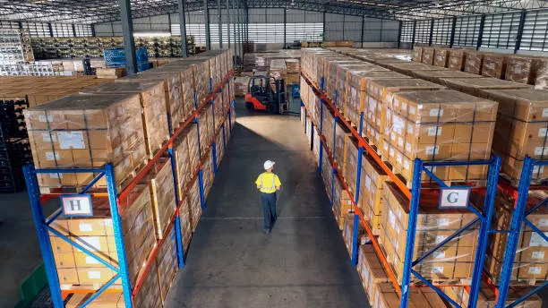 A high-angle view of a vast warehouse with tall blue storage racks labeled 'H' and 'G' holding stacked boxes