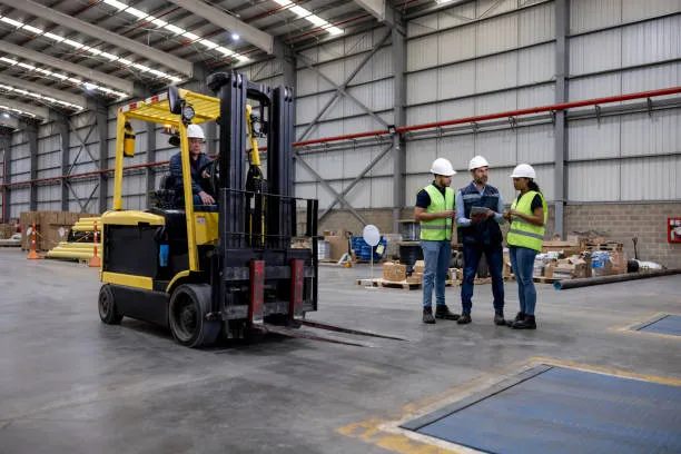 A yellow forklift operator in a hard hat moving through a large warehouse