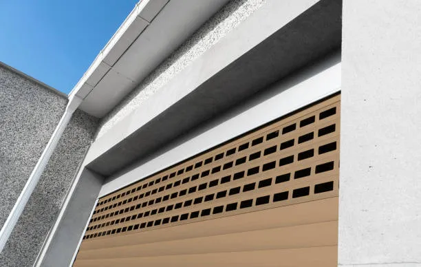 A low-angle view of a tan perforated roller shutter door installed on a modern concrete building