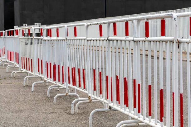 A row of interconnected white metal crowd control barriers with red reflective stripes