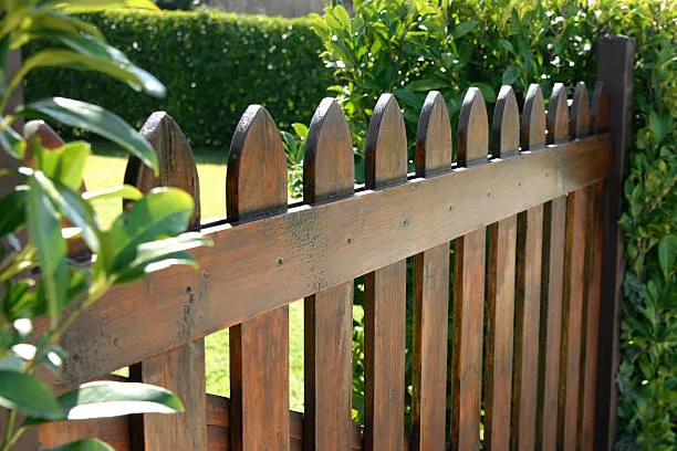 A dark-stained wooden picket fence with pointed gothic-style tops