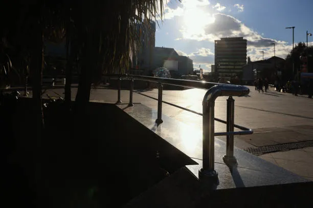 A polished stainless steel handrail reflects the bright afternoon sun in a public plaza