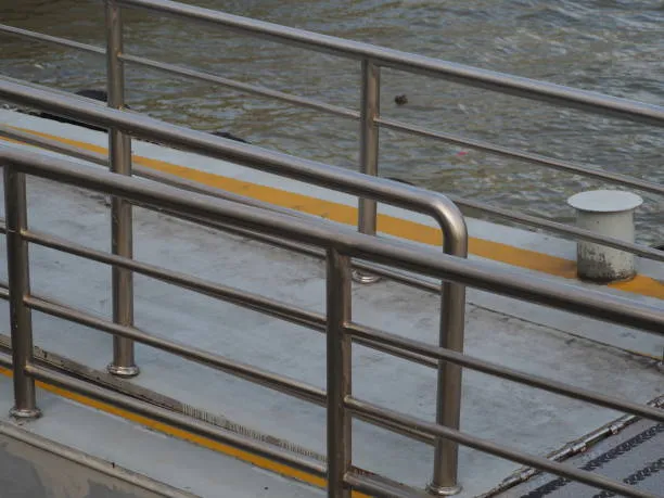 A close-up view of stainless steel safety railings along a concrete walkway or pier next to water