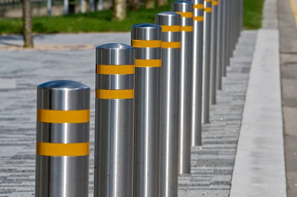 A row of sleek, stainless steel security bollards with double yellow reflective stripes