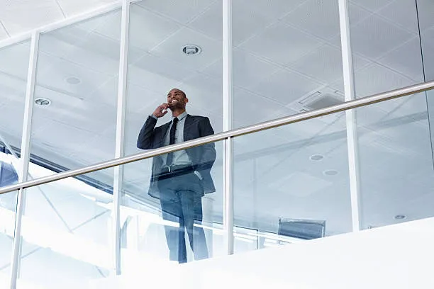 Businessman on glass office balcony talking on phone