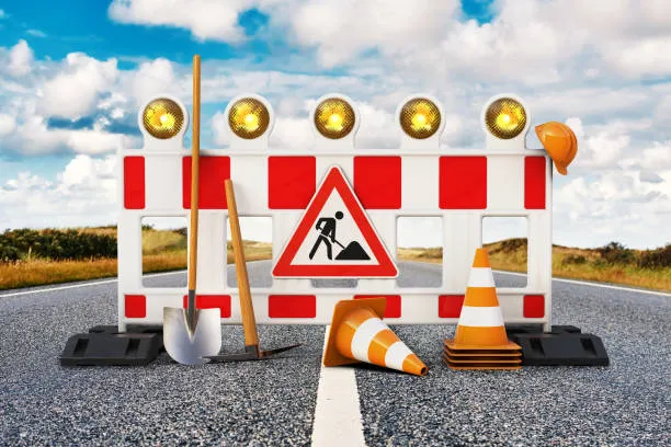 A red and white striped road construction barrier with flashing yellow lights and a 'men at work' sign